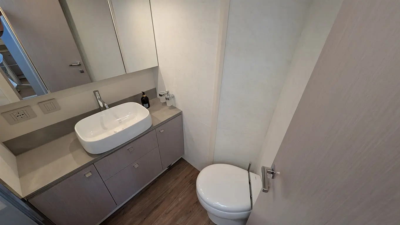 Modern bathroom featuring a basin, toilet, wooden flooring, and large mirrors reflecting the space.